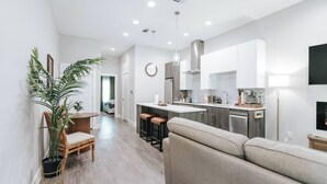 A modern kitchen with white cabinets, a central island, and a dining area with a table and chairs. - Modern Condo Near Downtown Fort Worth & Stockyards (Fort Worth)