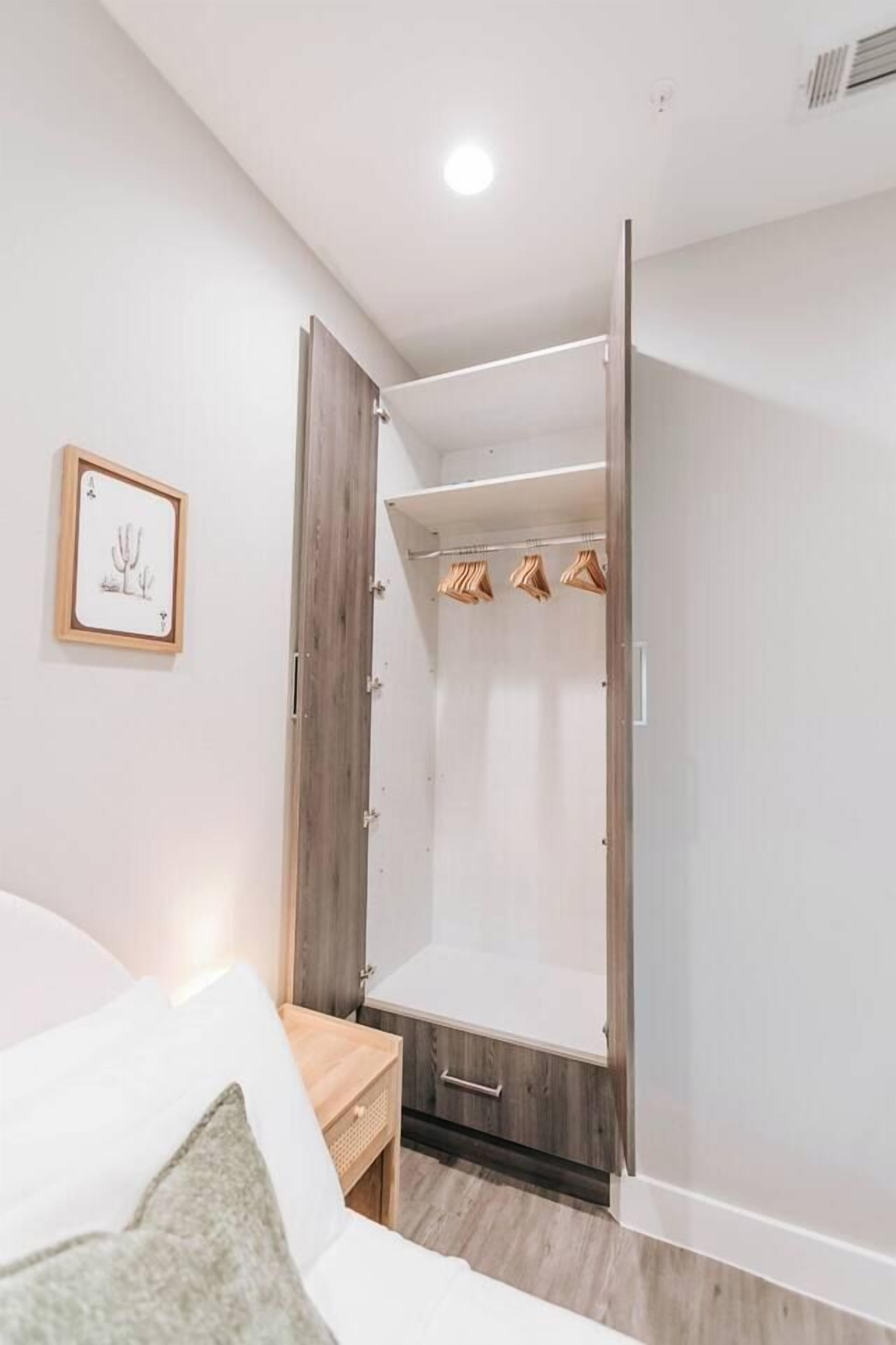 A bedroom with a bed, a nightstand, a wardrobe, and a framed picture on the wall.