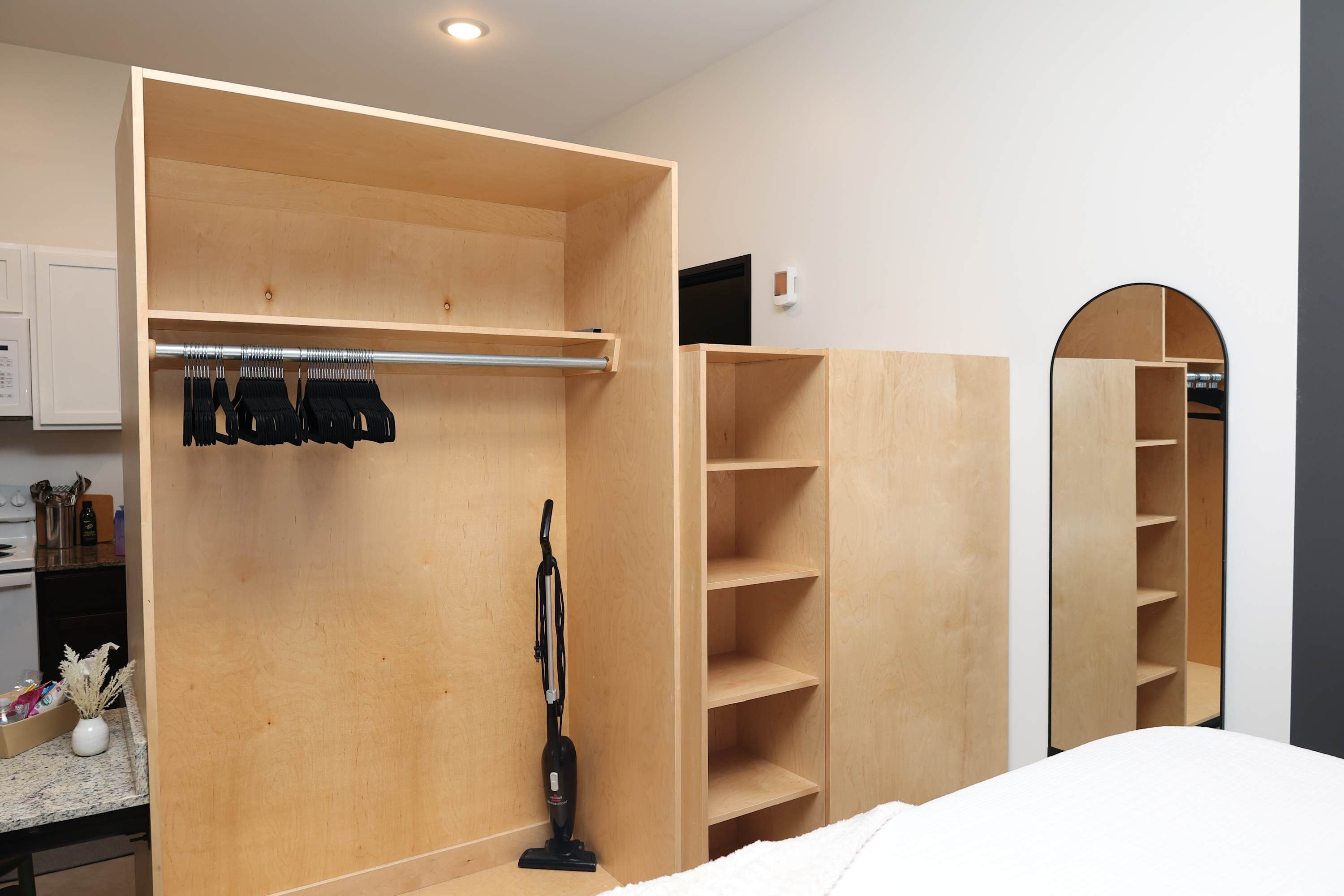 A room with a wooden wardrobe, a vacuum cleaner, and a mirror.