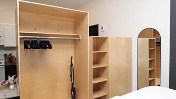 A room with a wooden wardrobe, a vacuum cleaner, and a mirror.