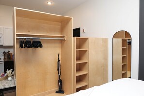 A room with a wooden wardrobe, a vacuum cleaner, and a mirror.