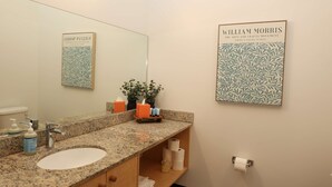 A bathroom with a granite countertop sink, a large mirror, a toilet, and a framed artwork on the wall.