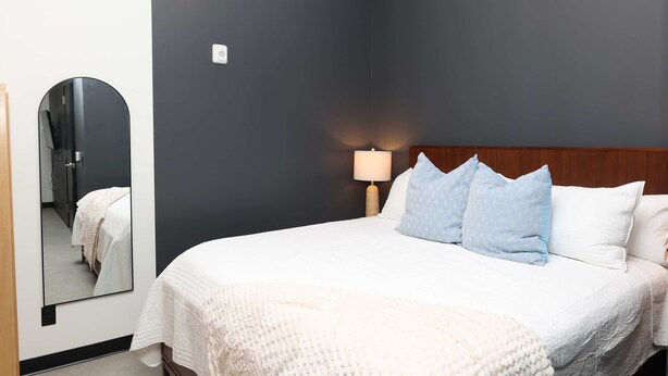 A hotel room with a large bed, a bedside lamp, a mirror, and a wooden headboard.