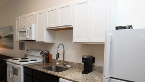 A kitchen with white cabinets, a microwave, a stove, a coffee maker, and a dishwasher.