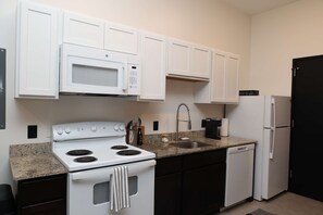 A kitchen with white cabinets, a stove, a microwave, a sink, and a refrigerator.