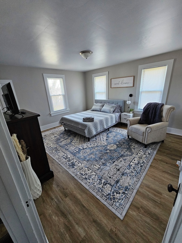 A bedroom with a bed, nightstand, chair, and a desk with a computer.