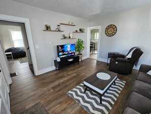 A living room with a TV, sofa, coffee table, and a clock on the wall. - Serene 2-bedroom house in adorable Malvern (Malvern)