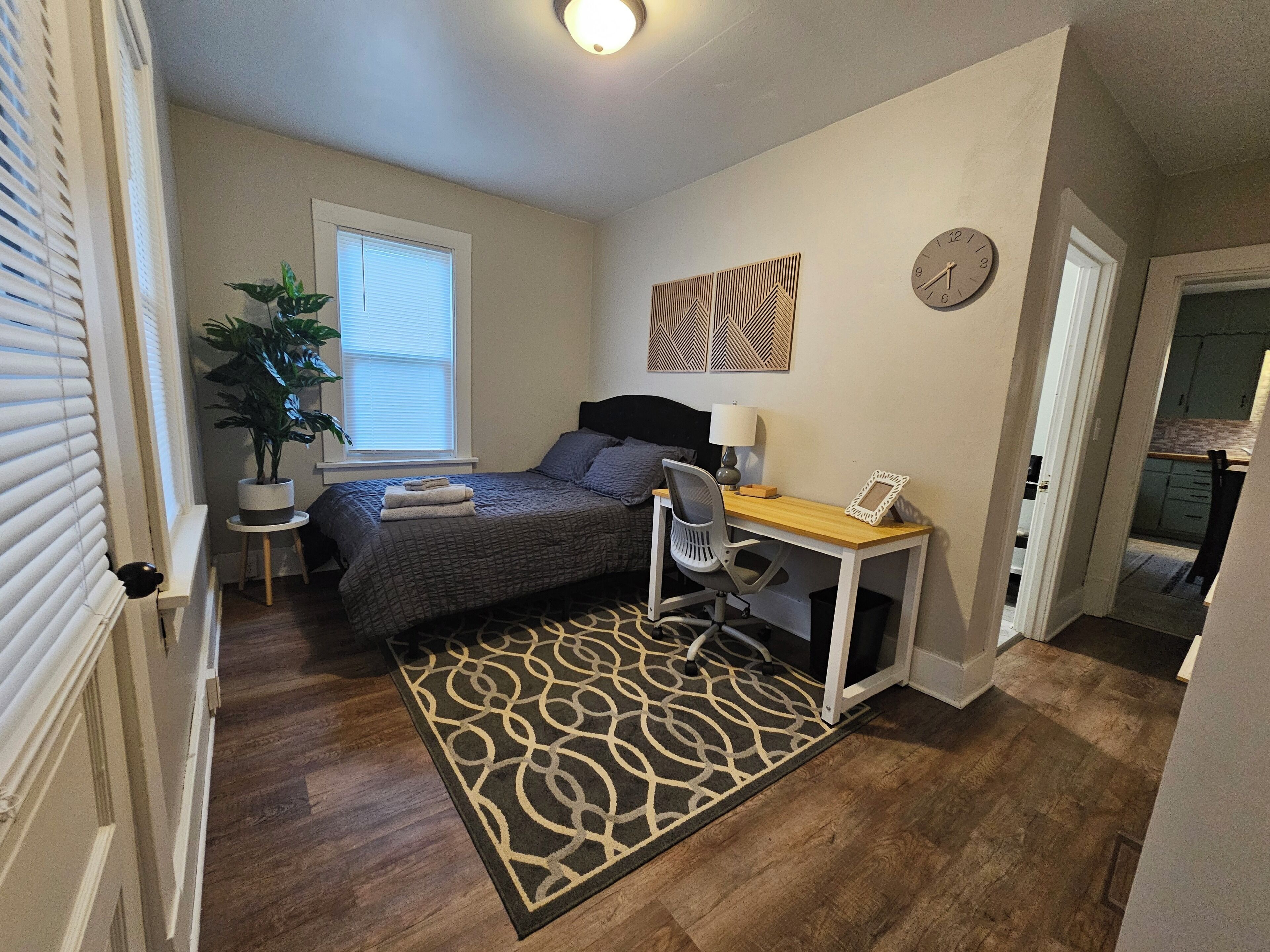 A compact bedroom with a bed, bedside table, lamp, chair, and a small desk.