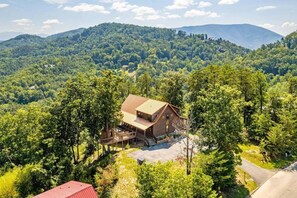 A cabin with a wooden exterior, a deck, and a view of a forested mountain range. - Mountain View Retreat | Perfect for Groups, Events & Getaways (Sevierville)
