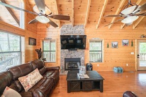 A log cabin interior with a stone fireplace, leather sofa, and ceiling fans. - Mountain View Retreat | Perfect for Groups, Events & Getaways (Sevierville)