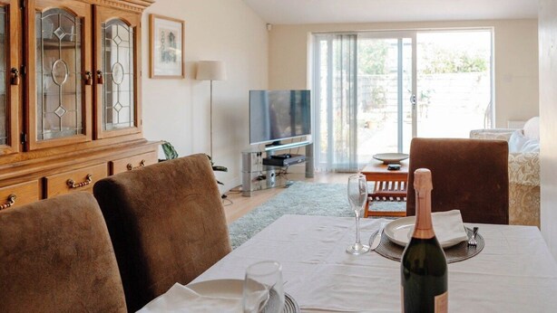 Comedor con una mesa lista para dos, una botella de vino y un televisor al fondo.