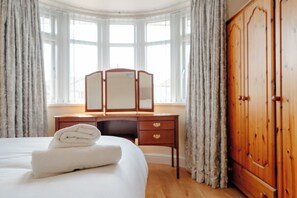 Ein Hotelzimmer mit Bett, einem Holzschrank, einem Schreibtisch mit Spiegel und einem fenster mit Vorhängen.