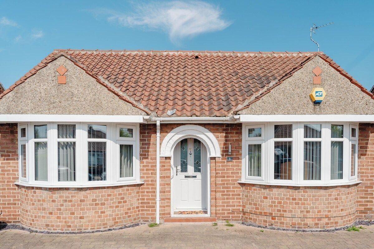 A two-story brick house with a tiled roof, a white front door, and two bay windows.