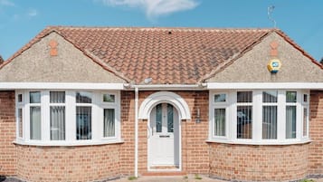 A two-story brick house with a tiled roof, a white front door, and two bay windows.