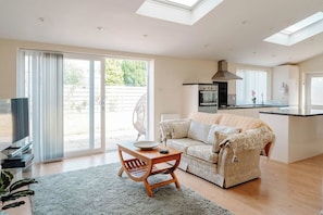 A modern living room with a sofa, a coffee table, and a TV. There is a sliding glass door leading to an outdoor area. - Spacious Garden Home | Near York | Dog Friendly (York)