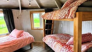 Quarto com beliche, escada, janela e cama com travesseiro rosa.