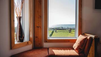 Habitación en esquina con un banco de madera, un florero con ramas y vistas a una cerca y al agua.