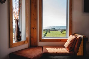 A corner room with a wooden bench, a vase with branches, and a view of a fence and water.
