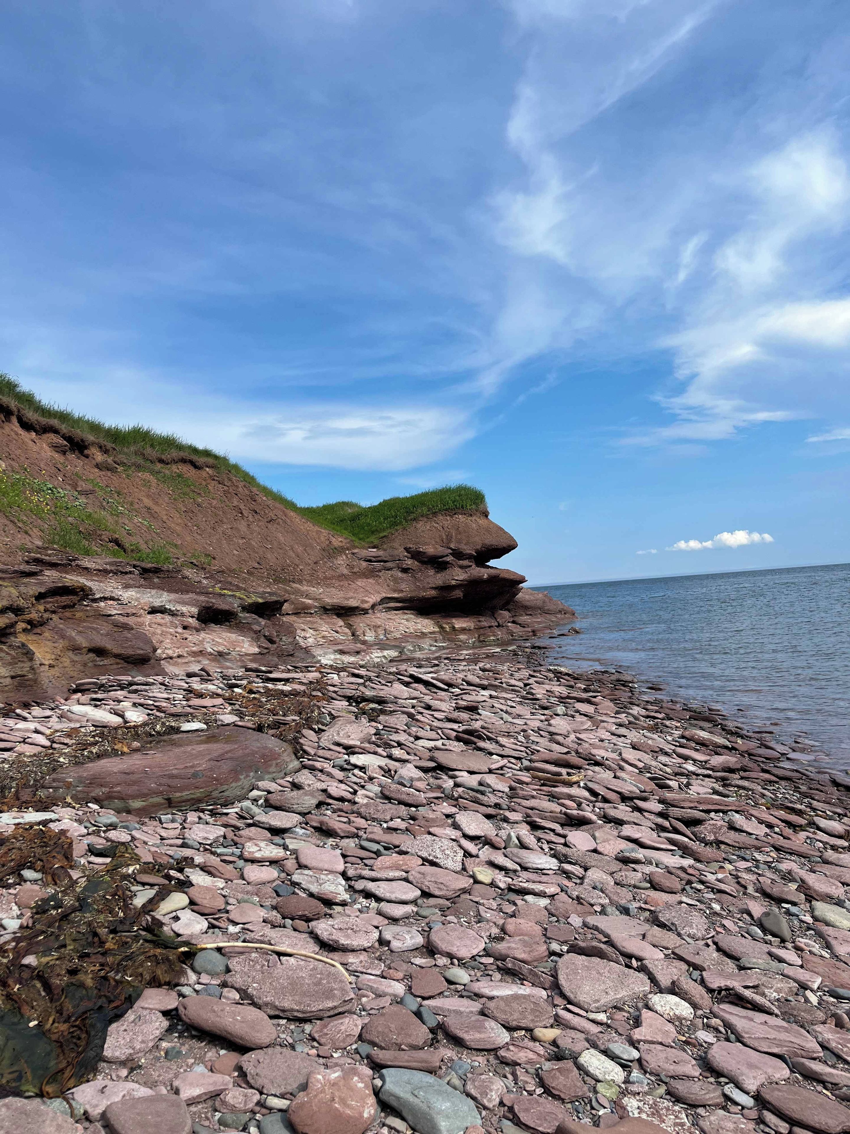 Eine felsige Küstenlinie mit einer grasbewachsenen Klippe und ruhigem Wasser.