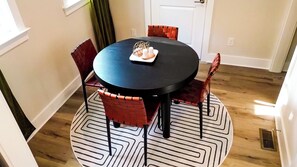A round dining table with a black top, surrounded by four red chairs with a woven pattern. A white tray with candles is placed on the table. - Raleigh Modern - Stylish 4BR - 5 TVs - Downtown (Raleigh)