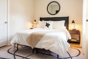 A neatly made bed with a headboard, a bedside lamp, and a small bedside table with a book. - Raleigh Modern - Stylish 4BR - 5 TVs - Downtown (Raleigh)