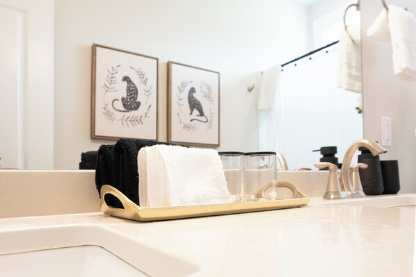 A bathroom with a sink, two framed wall art pieces, a towel rack, and a tray with glasses. - Raleigh Modern - Stylish 4BR - 5 TVs - Downtown (Raleigh)
