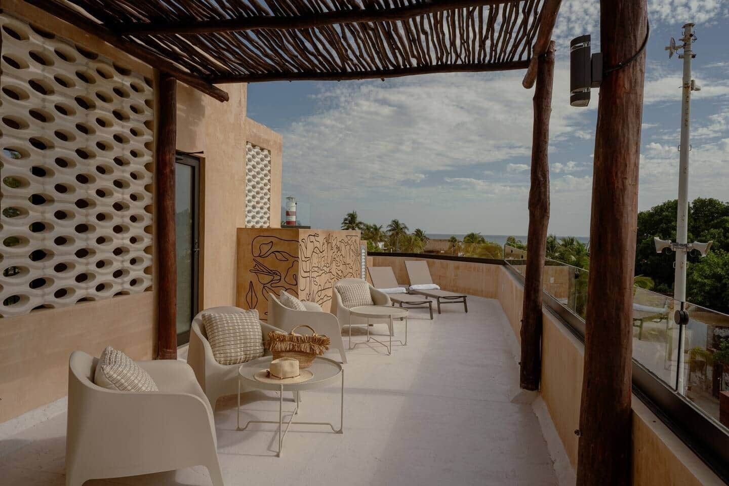 A rooftop terrace with white chairs, a small round table, and a view of the ocean.