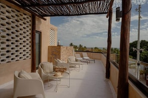 A rooftop terrace with white chairs, a small round table, and a view of the ocean.