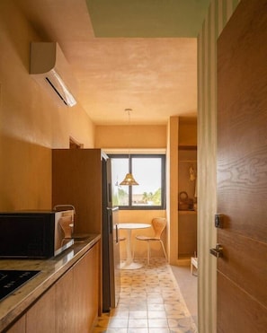 Cuina estreta amb finestra, zona de menjador amb taula i cadires, i una porta que dona a una altra habitació.
