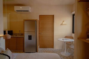 A compact hotel room with a bed, a kitchenette with a refrigerator, a dining area with a table and chairs, and a door. - Boutique studio steps from the sea • Rooftop • Pool (Sisal)
