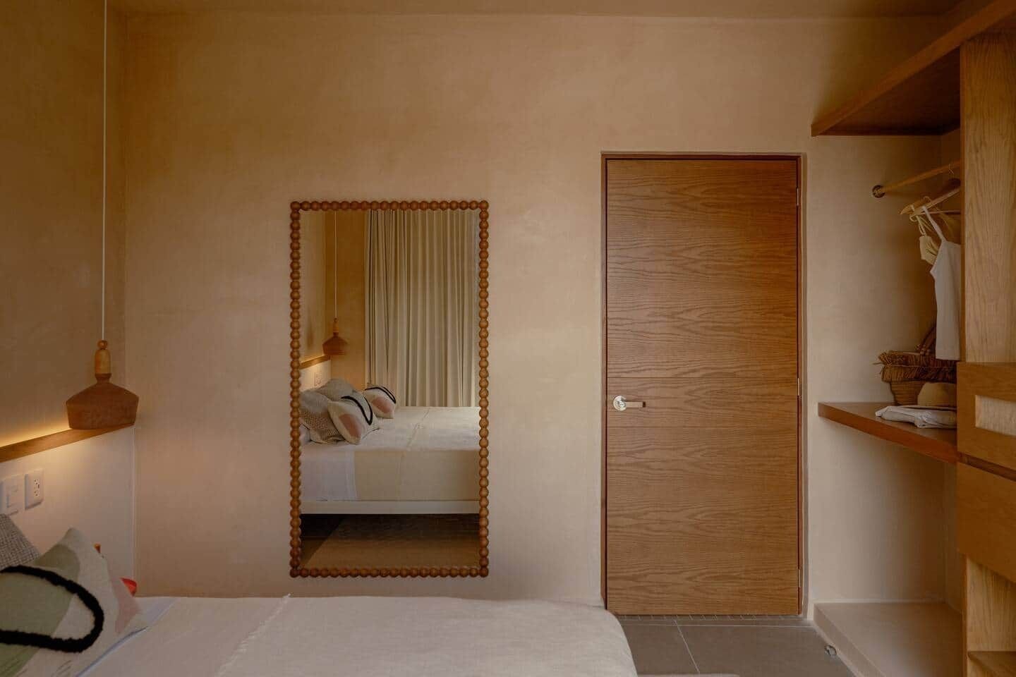 A bedroom with a bed, a wooden door, and a mirror with a bead frame.