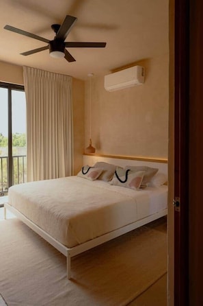 Um quarto com cama, ventilador de teto, janela com cortinas e ar-condicionado fixado na parede.