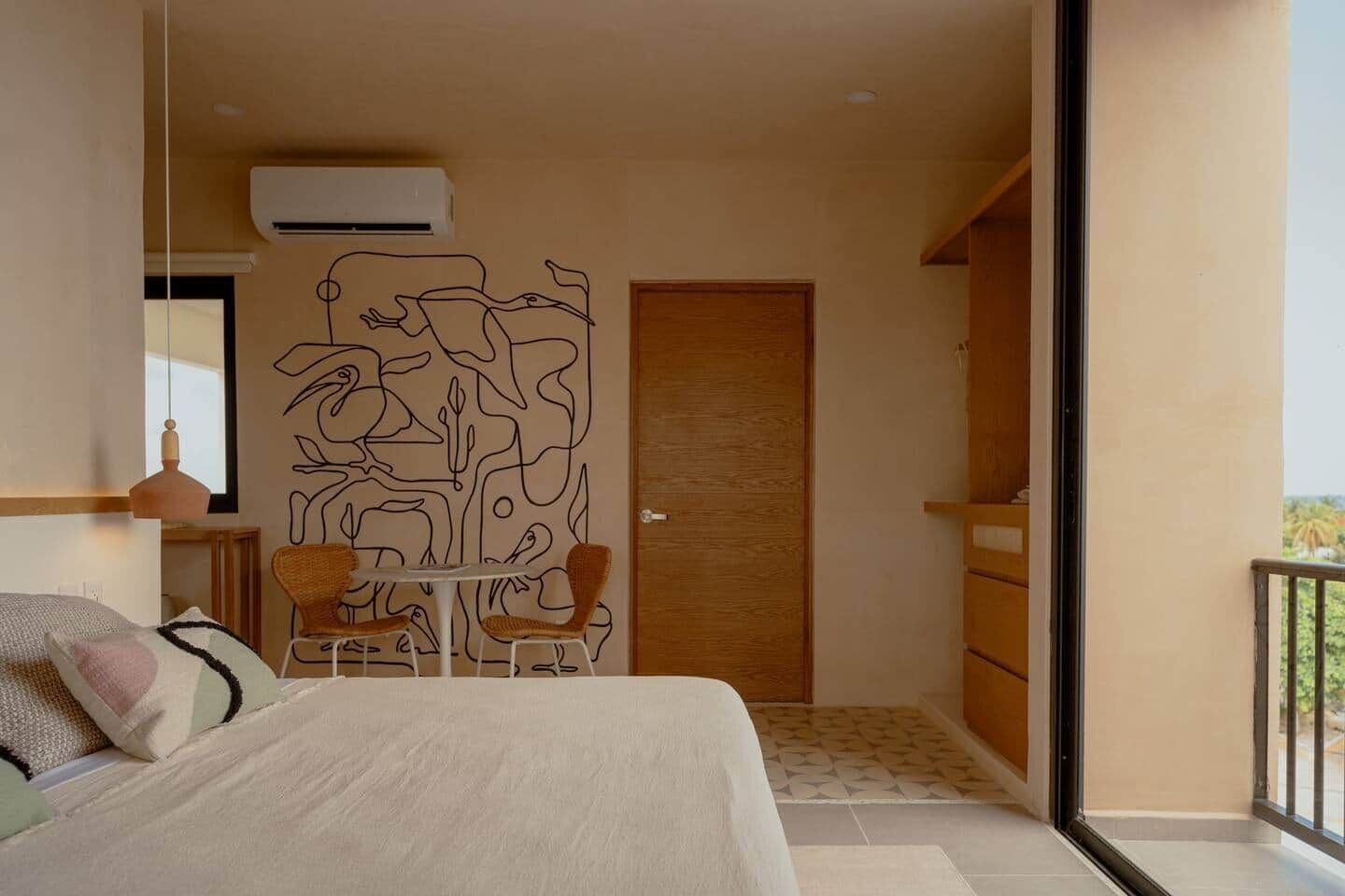 Une chambre à coucher avec un lit, une petite table avec des chaises, une œuvre d’art murale et une porte.