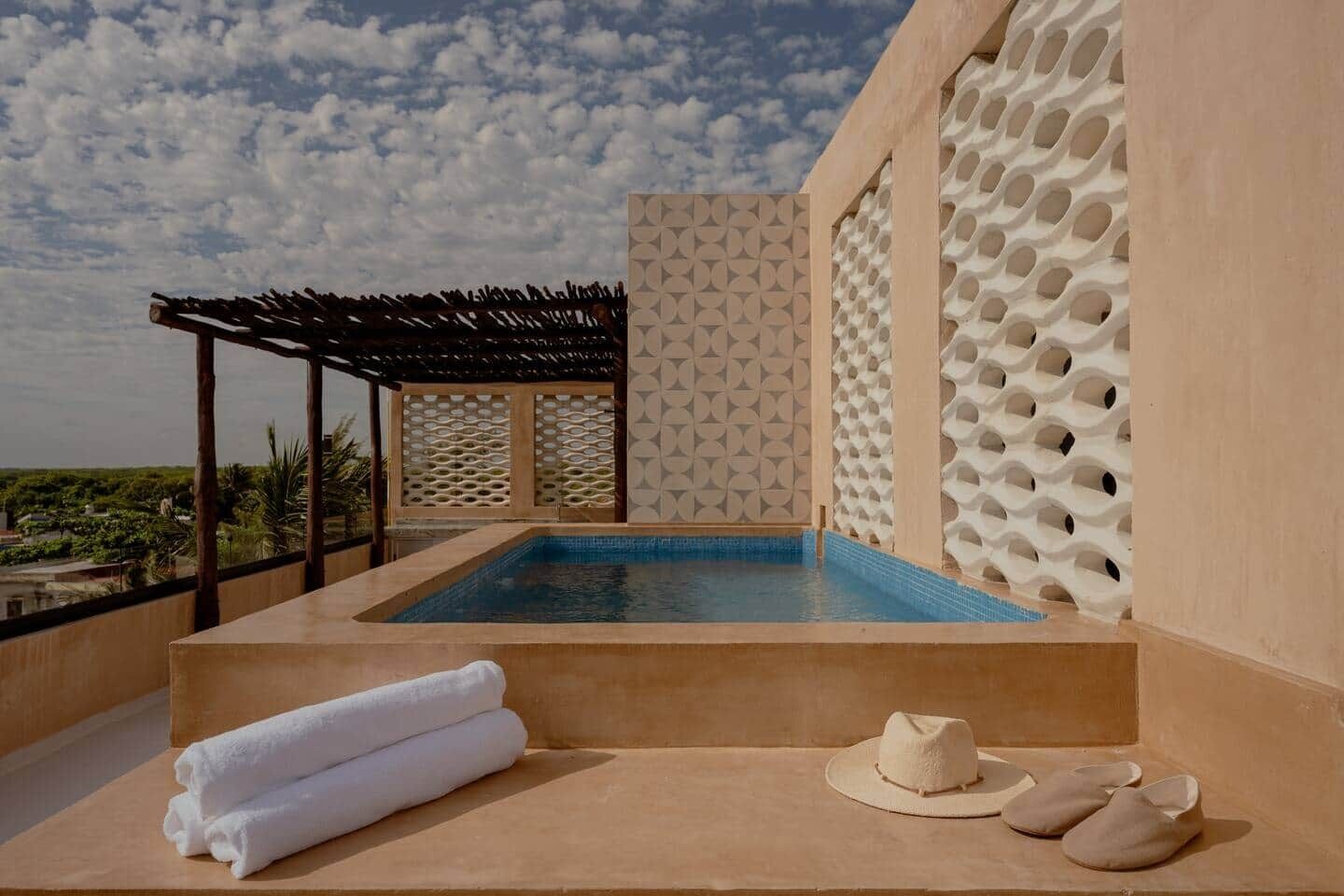 A rooftop pool area with a view of the landscape, a pergola, and a wall with a geometric pattern.