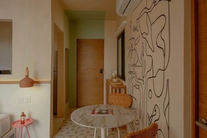 A room with a round table, a chair, a small stool, a wall with a black line drawing, and a door in the background. - Boutique Apartment with Ocean View • Rooftop with Pool (Sisal)