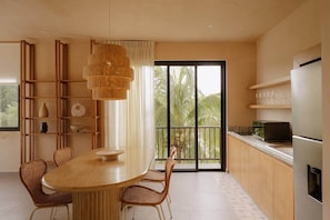 A modern kitchen with a dining table, chairs, a hanging light fixture, and a view of palm trees through large windows.