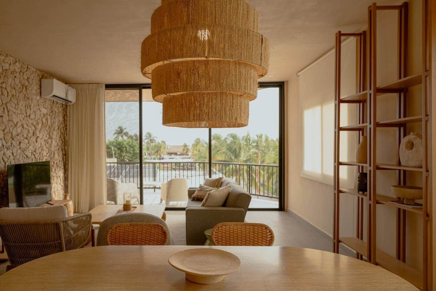 Ein modernes Wohnzimmer mit einem großen Fenster, Korbmöbeln und einem Holzbücherregal.