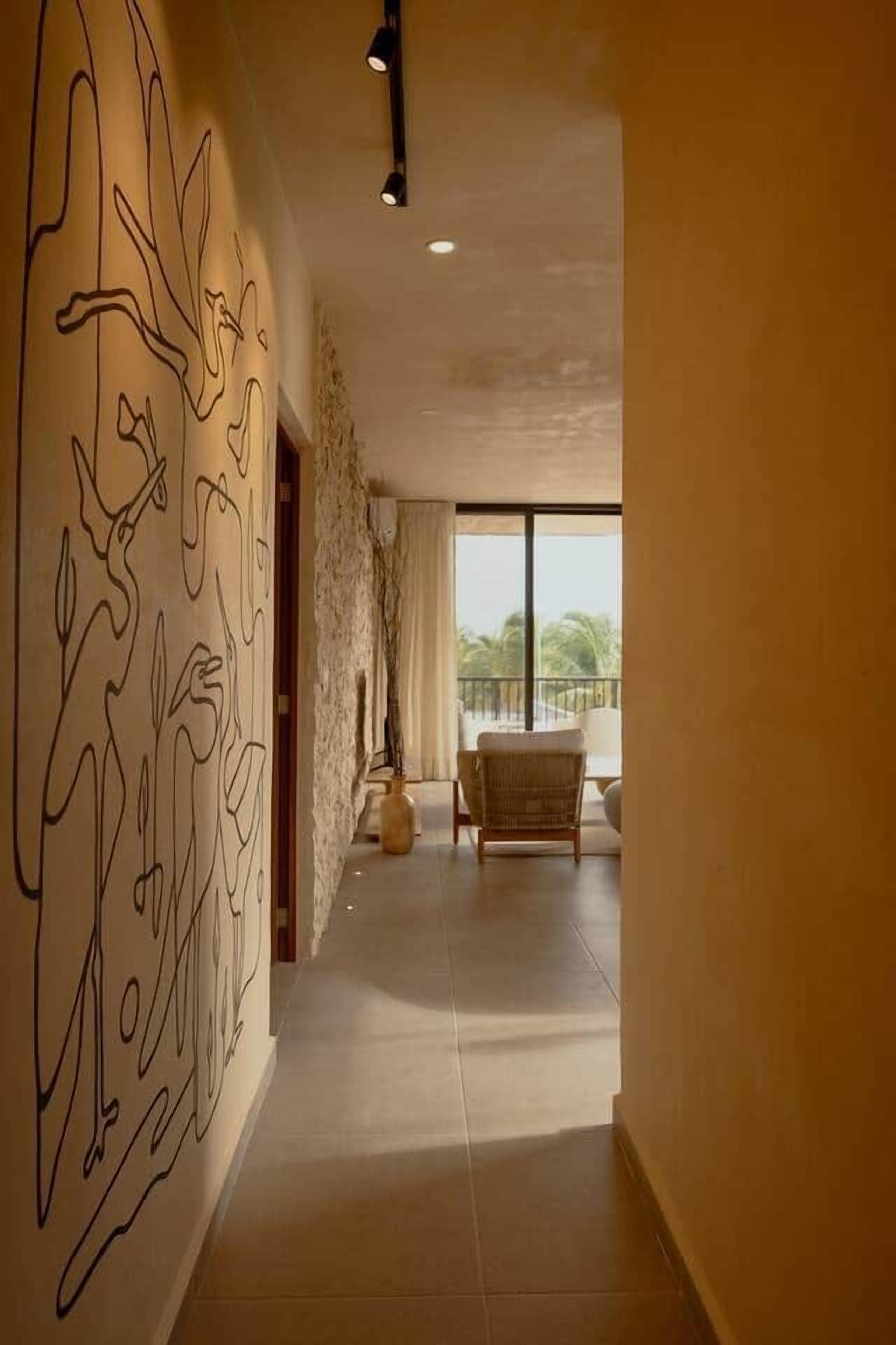 A corridor with a modern abstract wall art, leading to a balcony with a view of palm trees.