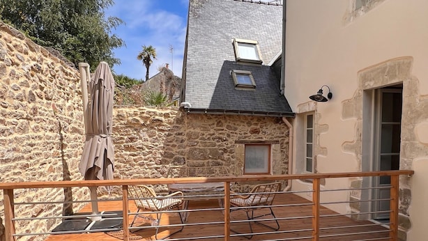 Un bâtiment en pierre doté d’une terrasse en bois, d’un espace extérieur aménagé pour s’asseoir et d’une petite fenêtre.