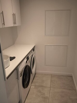 Une buanderie équipée d’un lave-linge, d’un sèche-linge et d’un plan de travail sur lequel se trouve un récipient.