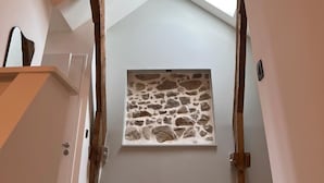 Un escalier avec des poutres en bois apparentes, un mur de pierre au motif texturé et un luminaire suspendu doté de plusieurs abat-jours.