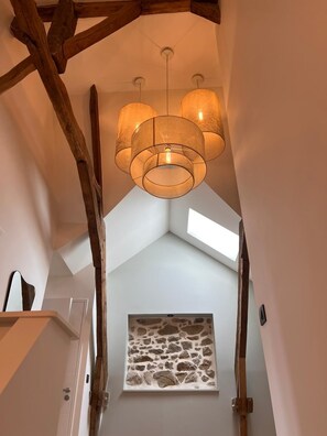 Un escalier avec des poutres en bois apparentes, un mur de pierre au motif texturé et un luminaire suspendu doté de plusieurs abat-jours.