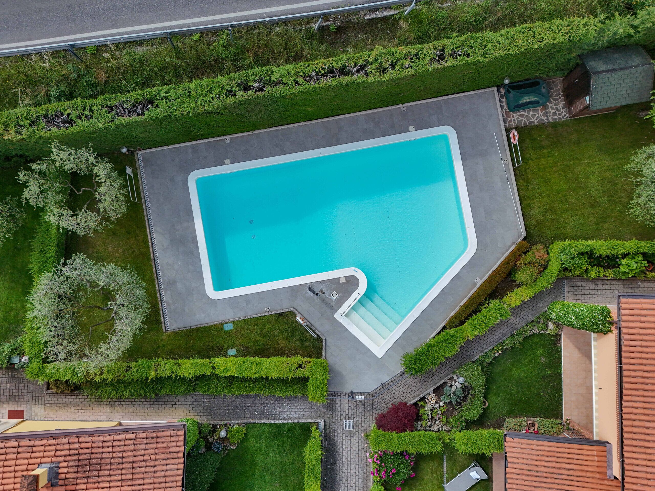 An aerial view of a swimming pool with a unique L-shaped design, surrounded by well-maintained lawns and hedges.