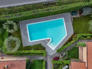 Eine Vogelperspektive eines Schwimmbeckens mit einem außergewöhnlichen L-förmigen Design, umgeben von gepflegten Rasenflächen und Hecken.