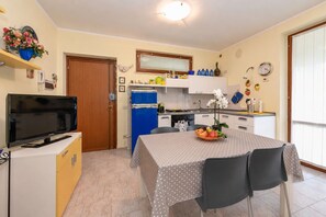 A compact kitchen with a dining table, chairs, a TV, and a blue refrigerator. - MGH - Garda Bloom Family Stay Manerba (Manerba del Garda)
