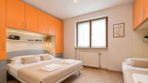 Et soveværelse med en seng, et sengebord, et vindue med gardiner, en radiator og orange skabe.