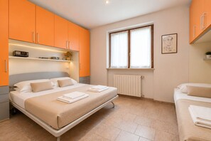 Ein Schlafzimmer mit einem Bett, einem Nachttisch, einem Fenster mit Vorhängen, einer Heizung und orangefarbenen Schränken.