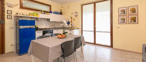 A compact kitchen with a blue refrigerator, a dining table with a polka dot tablecloth, and a fruit bowl.