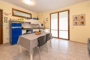A compact kitchen with a blue refrigerator, a dining table with a polka dot tablecloth, and a fruit bowl. - MGH - Garda Bloom Family Stay Manerba (Manerba del Garda)