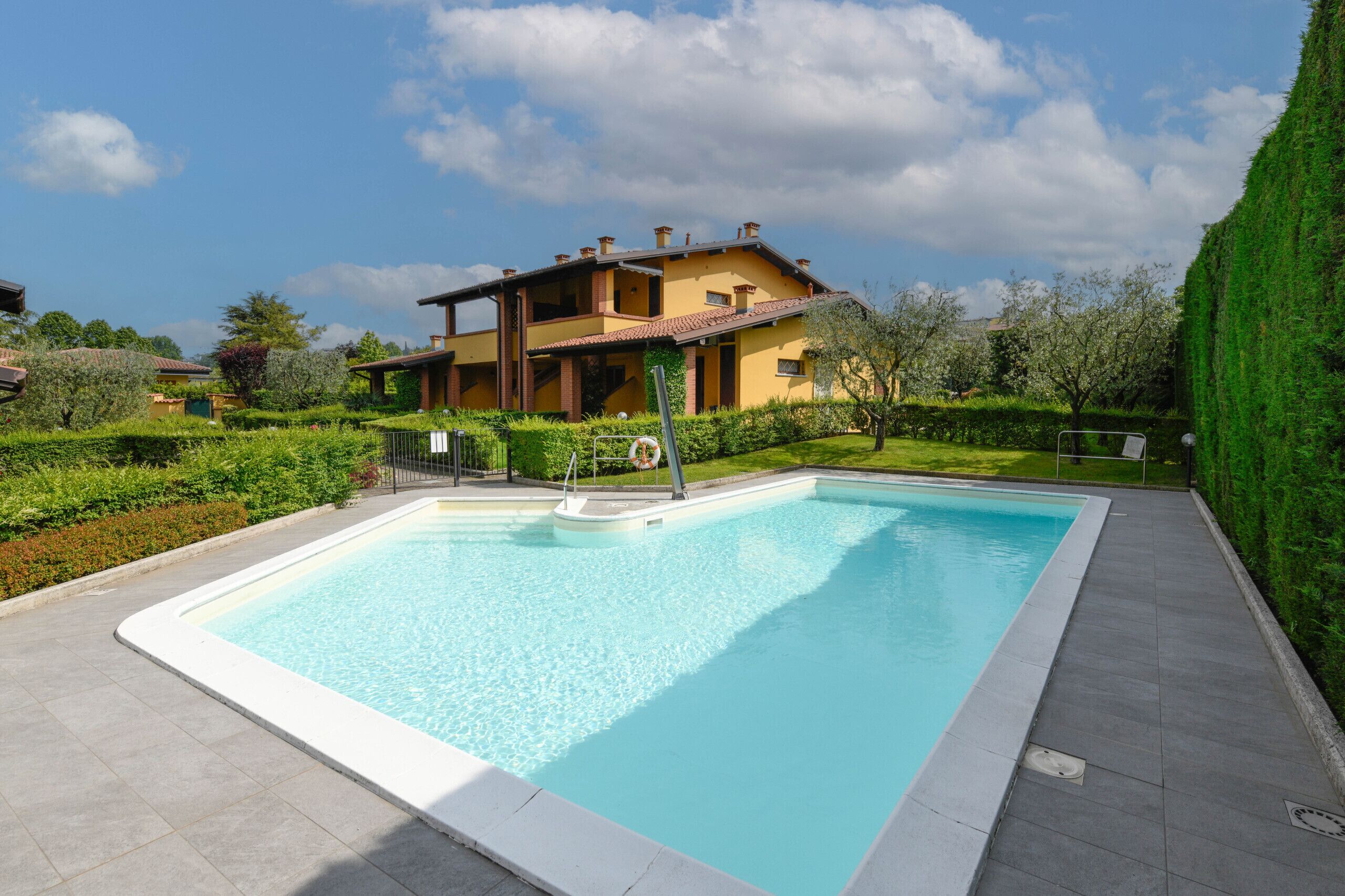 A rectangular swimming pool with a lifebuoy and a metal ladder, surrounded by a paved deck.